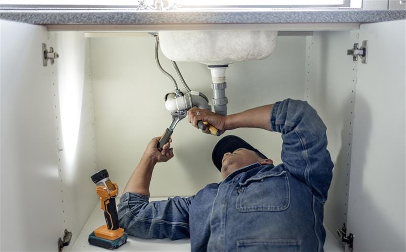 Plumber repairing pipes beneath a bathroom sink in San Gabriel